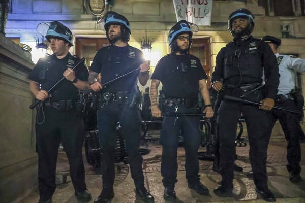 Four police officers standing in uniforms and baby blue helmets holding nightsticks and looking well pleased with themselves
