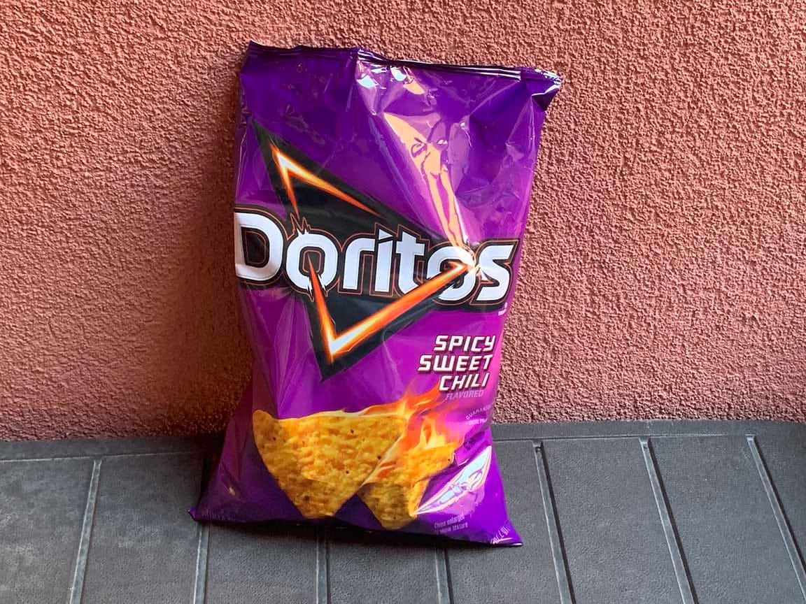 A very purple bag of SPICY SWEET CHILI Doritos, with product art of some Dorito-triangles in flames.