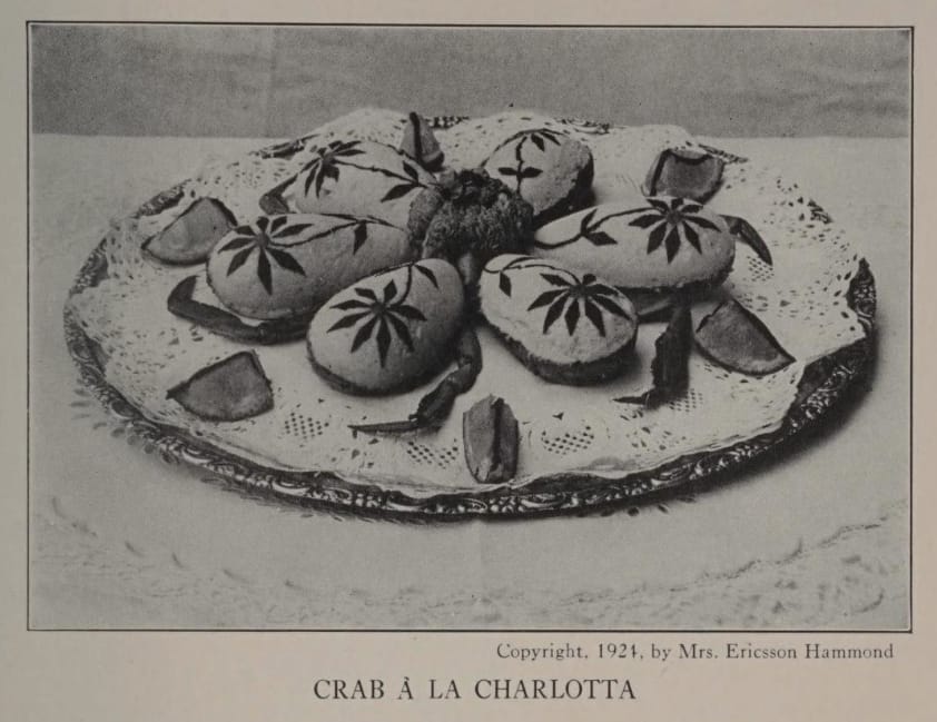 Crab à la Carlotta photo from "Mrs. Ericsson Hammond's Salad Appetizer Cook Book," six small, teardrop-shaped sandwiches with ornate floral deorations on each sandwich top, arranged in a flower shape, crab legs and pieces of lemon circling the whole thing. Photo by Mrs. Ericsson Hammond