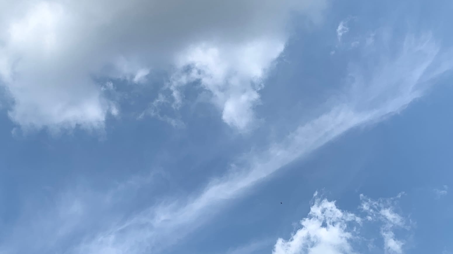 A wispy diagonal-line of cloud separating a gig cloud and a scruffy little cloud in opposing corners of the frame