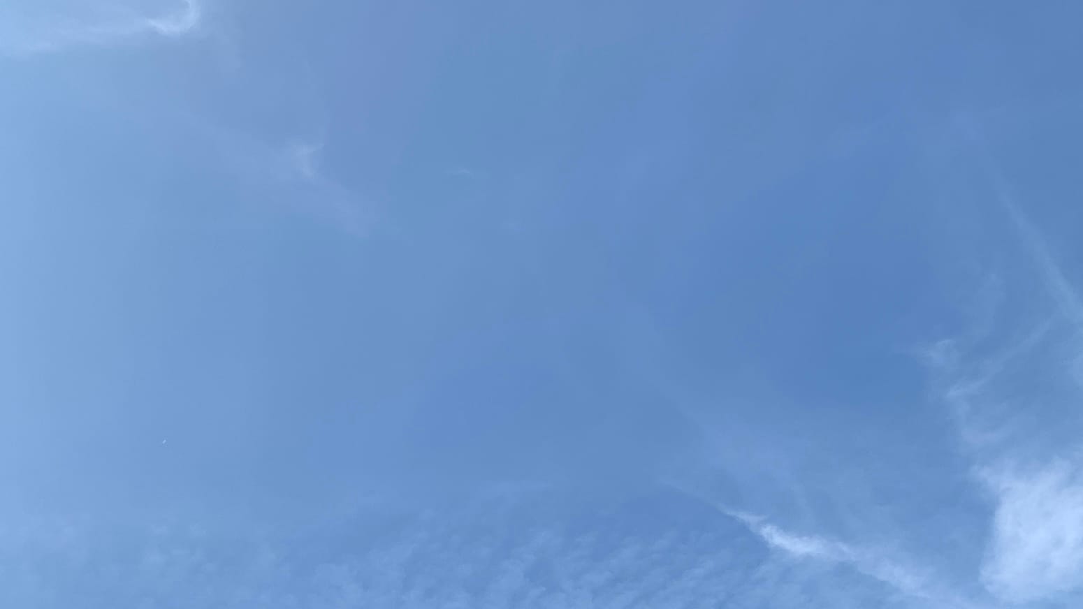 Blue sky with a few high wisps of cloud, some in faint furrows, in the upper left and lower right corners