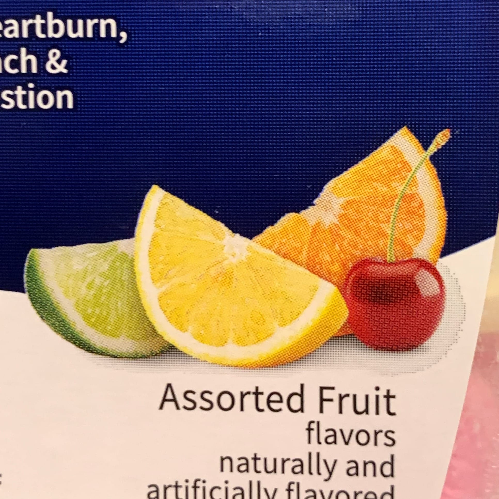 Closeup crop of label, ASSORTED FRUIT FLAVORS NATURALLY AND ARTIFICIALLY FLAVORED, "stock-photo-style still life of a cherry, an orange wedge, a lemon wedge, and, peeking out from behind, a wedge of lime."