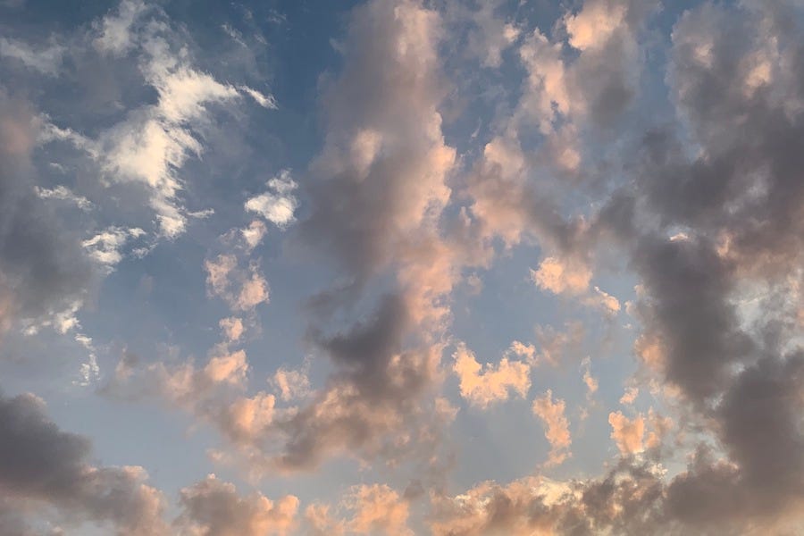 A blue sky filled with a jumbled assortment of clouds like short brushstrokes in white, gray, gold, and pink.