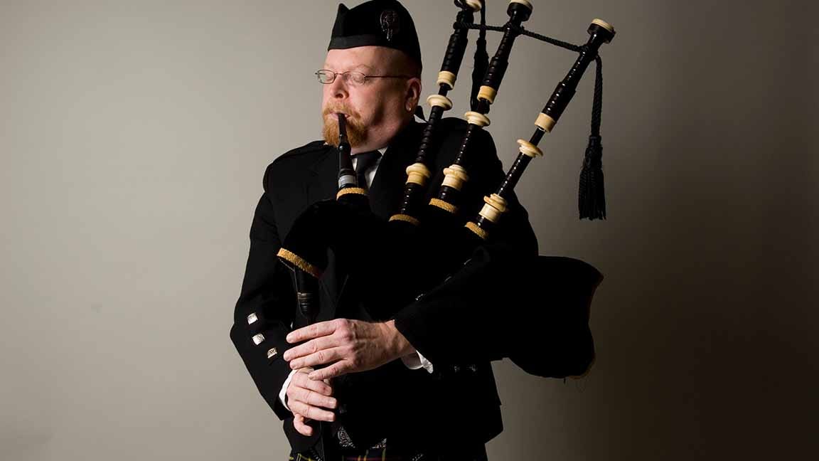 A man with traditional bagpipe clothing playing bagpipes