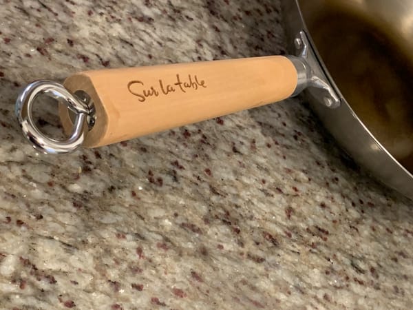 Wooden "Sur la table" wok handle, on a silver wok, on a gray granite coun