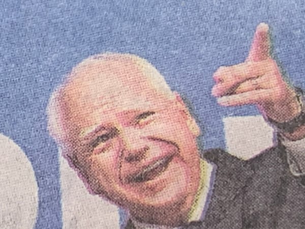 Detail of New York Times print edition photo of Tim Walz smiling and pointing against a blue background