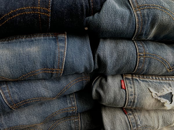 Two piles of folded dungarees going from dark blue and new-looking to faded and ripped