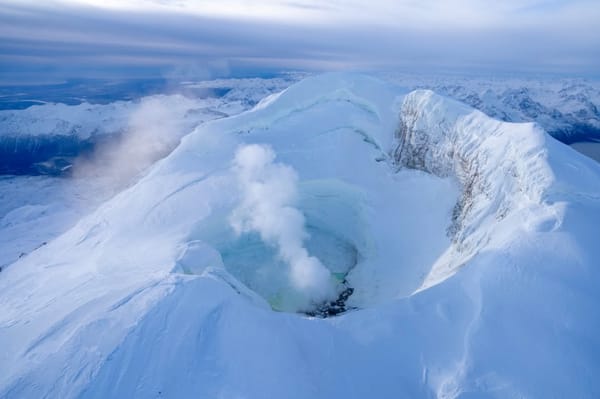 A deeply snow-and-ice-clad summit in the foreground, with a valley backed by many more snowy mountains.